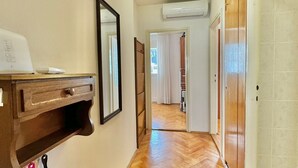 A hallway with a wooden floor, a wall-mounted shelf with a mirror, and an air conditioning unit. - Family two bedroom apartment Slavia (Budva)