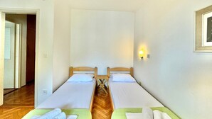 A room with two single beds, a wooden floor, a wall-mounted light, and a door leading to another room. - Family two bedroom apartment Slavia (Budva)
