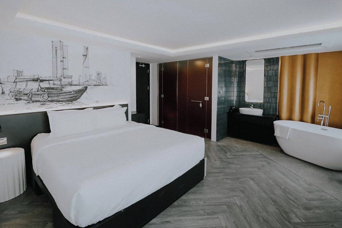 A modern hotel room with a large bed, a bathroom with a bathtub, and a mural of a ship on the wall.