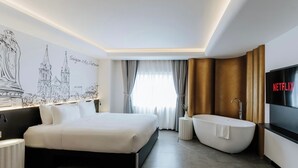 Una camera d'albergo moderna con un letto grande, una vasca da bagno, una TV a parete e un murale raffigurante un paesaggio urbano.