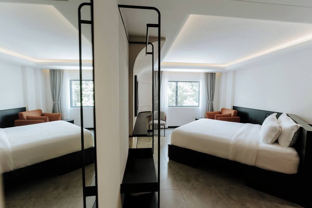 A modern hotel room with two beds, a desk, and a chair.