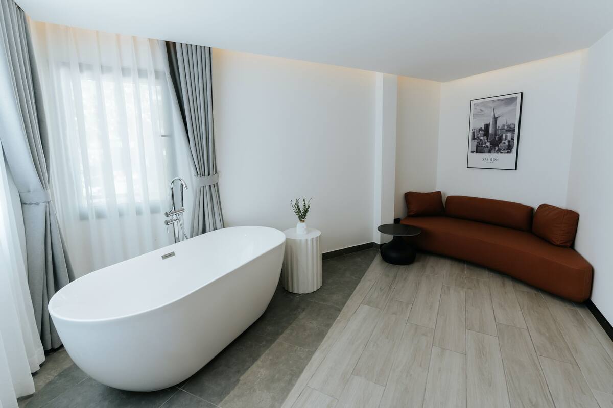 A modern bathroom with a freestanding bathtub, a small round table, and a brown sofa.