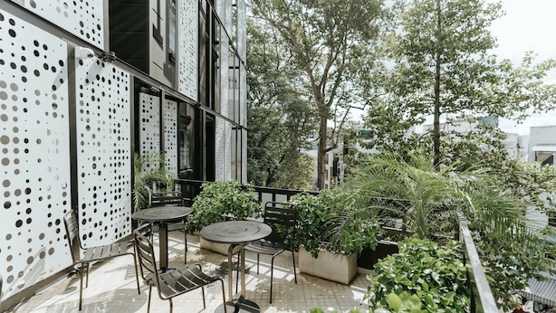 Patio esterno con tavolo e sedie, circondato da piante in vaso e alberi.