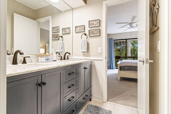 A bathroom with a double sink, dark cabinets, and a mirror. There are towels hanging on hooks and a shower curtain visible in the background.