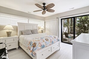 Une chambre à coucher avec un lit, des tables de chevet, un ventilateur de plafond et une vue sur l’extérieur.