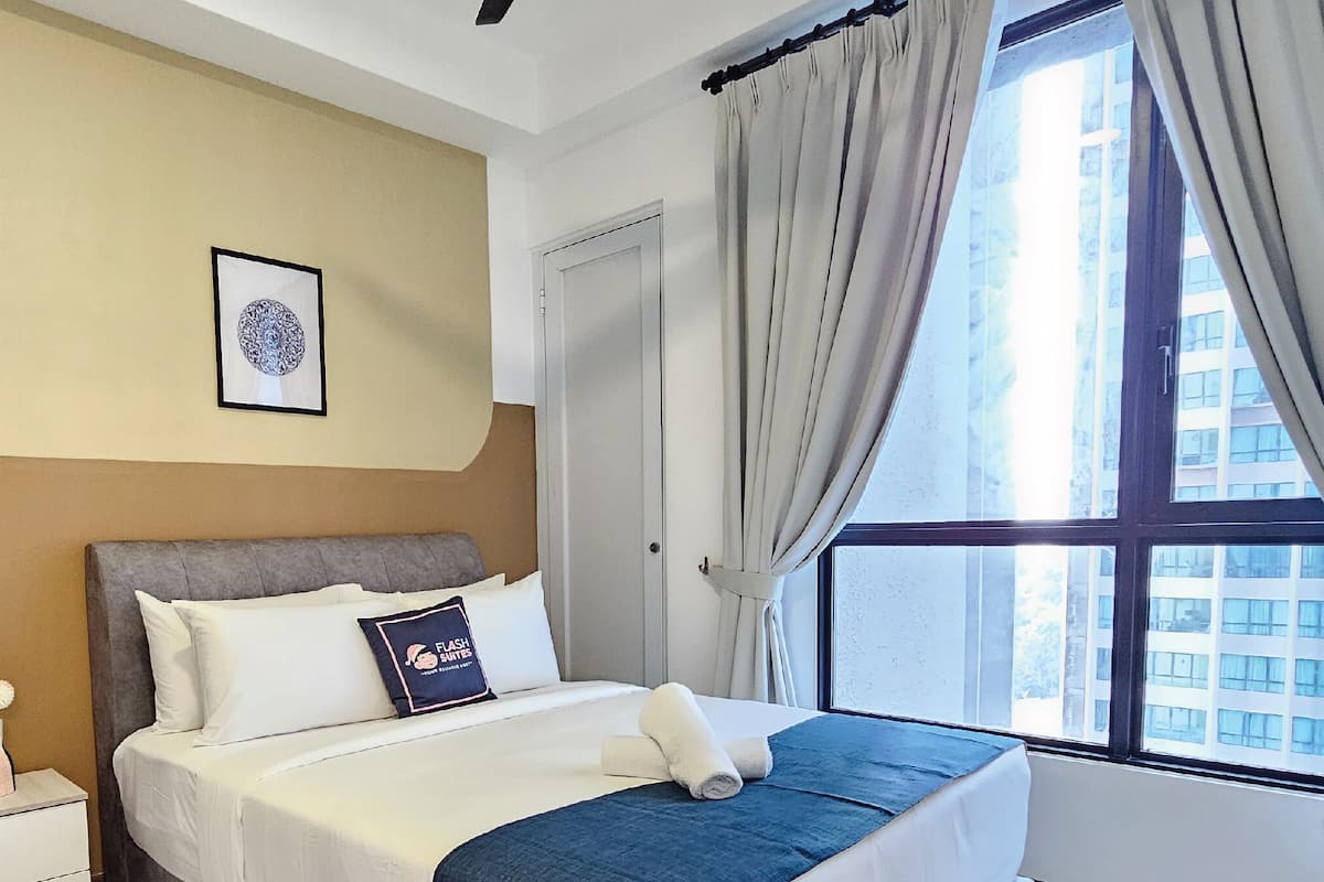 A hotel room with a bed, a nightstand, a framed picture, and a window with curtains.