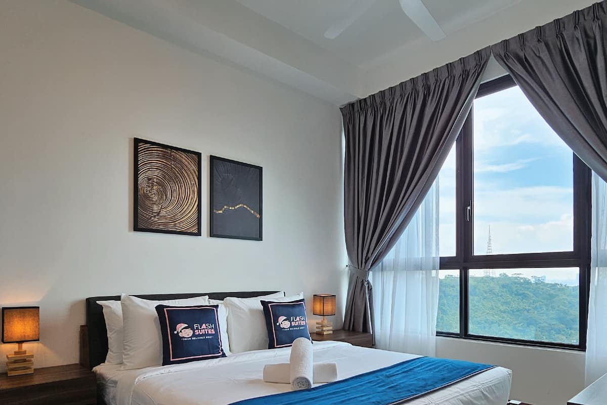 A hotel room with a bed, two bedside lamps, a window with curtains, and two framed artworks on the wall.