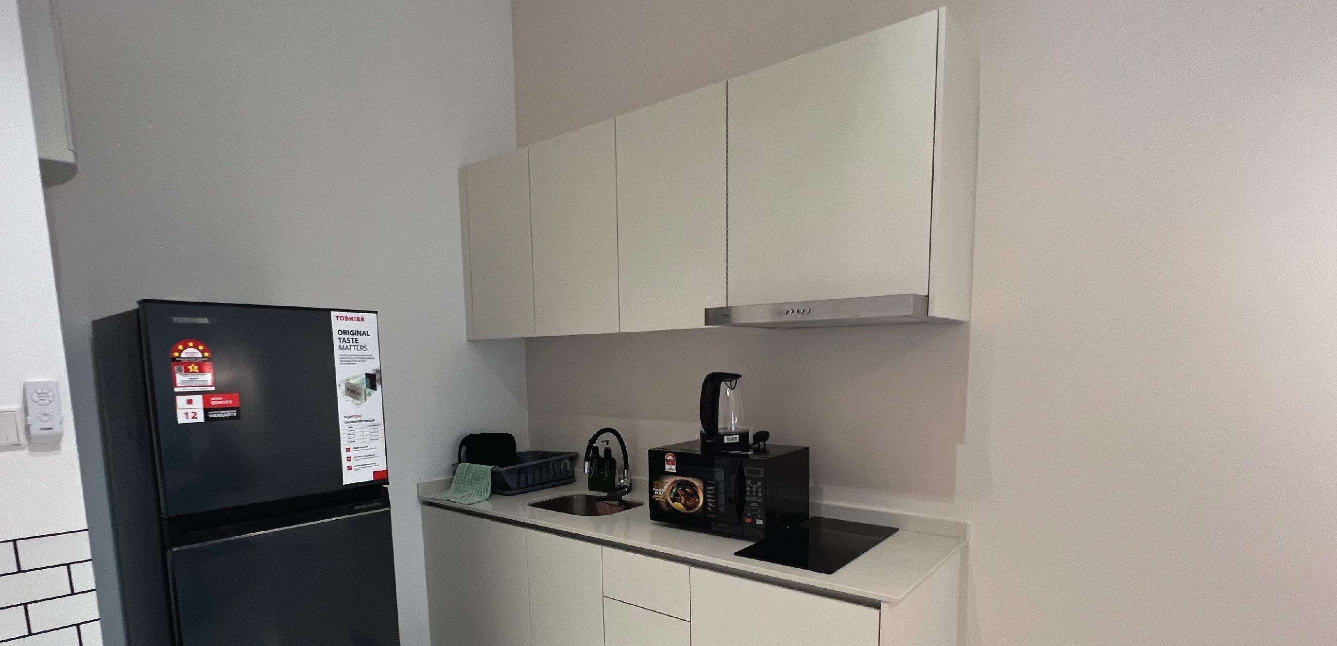Cocina compacta con refrigerador, microondas, hervidor y cafetera sobre la encimera.