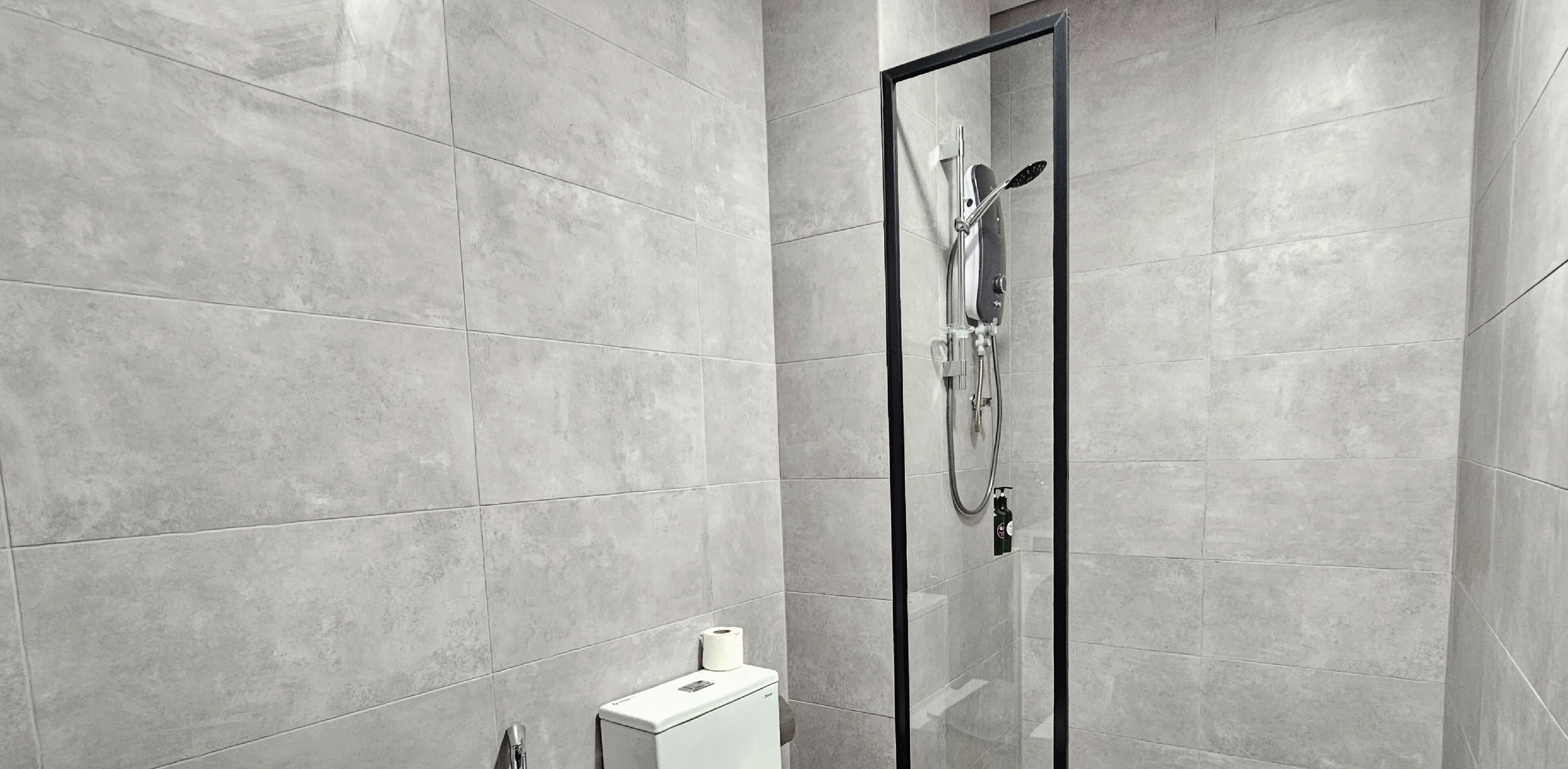 A modern bathroom with grey tiles, a glass-enclosed shower, and a toilet paper dispenser.