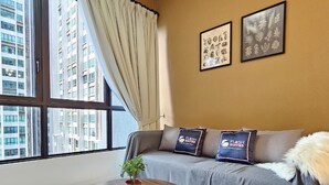 A modern hotel room with a large window, a grey sofa with branded pillows, and two framed botanical prints on the wall. - Cubic Botanical Premium Suites atBangsar (Kuala Lumpur)