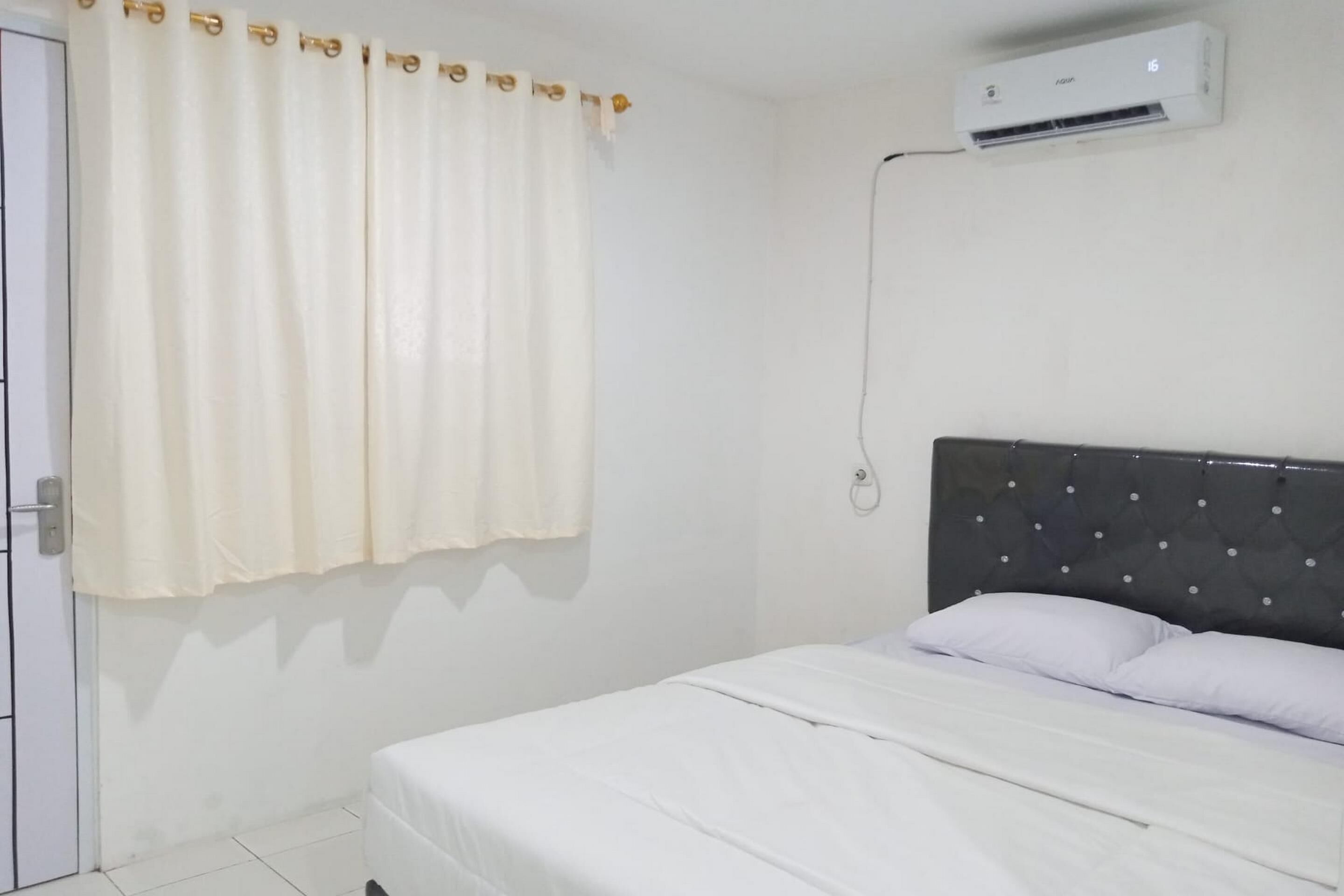 Un dormitori amb llit, cortines blanques, un aparell d'aire condicionat i una porta.