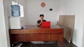 Una habitación con un escritorio de madera, un dispensador de agua, una caja roja y una botella de agua grande.