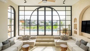 Un salón moderno con un amplio ventanal de arco que da a una piscina, sofás color beige y un ventilador de techo.