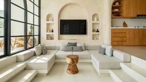 Una sala de estar moderna con un televisor grande, estanterías empotradas y una zona de cocina.