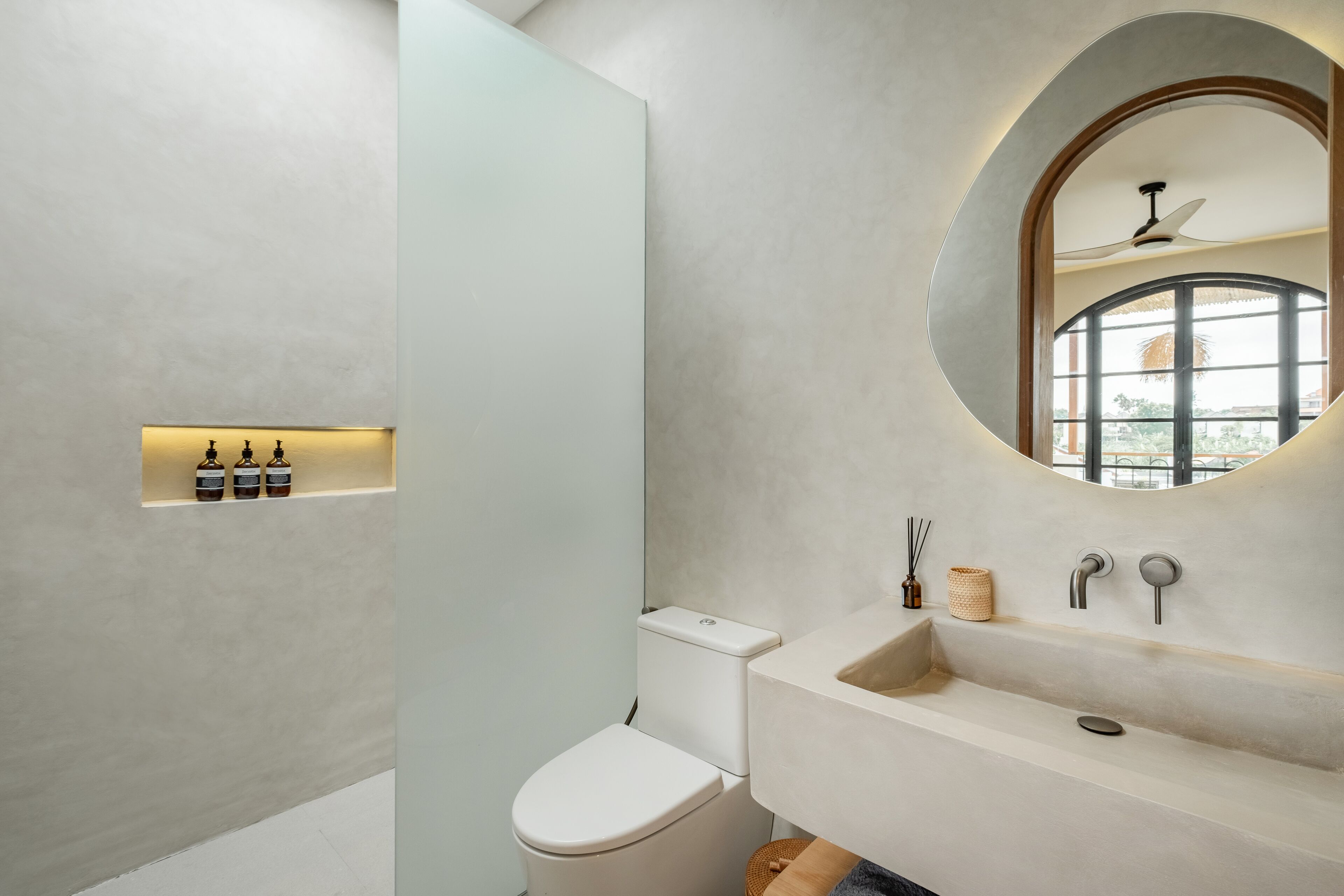 Une salle de bain moderne équipée de toilettes, d’un lavabo et d’un miroir placé au-dessus d’une fenêtre.