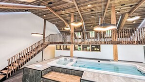 Un intérieur moderne avec un escalier en bois, un jacuzzi et un balcon doté d’une balustrade.