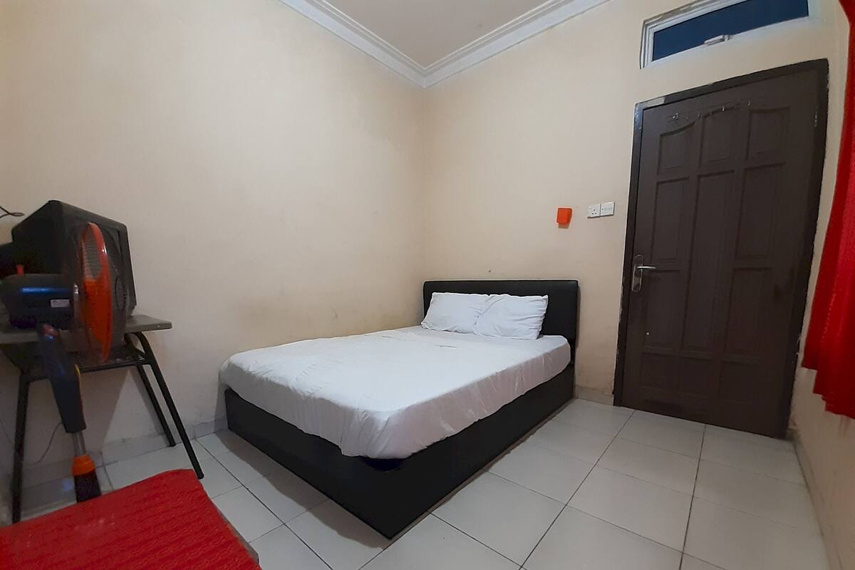 A bedroom with a bed, a desk with a computer, a chair, a door, and a window.