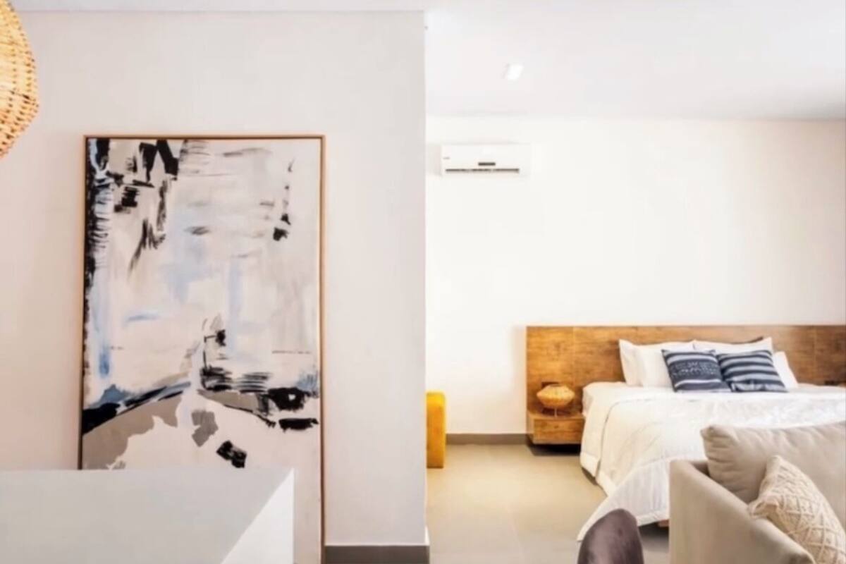 A modern hotel room with a large abstract painting on the wall, a bed with a wooden headboard, and a bedside table with a lamp.