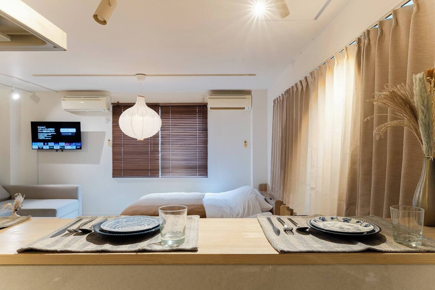 Habitación de hotel con cama, televisor montado en la pared y zona de comedor con mesa para dos.