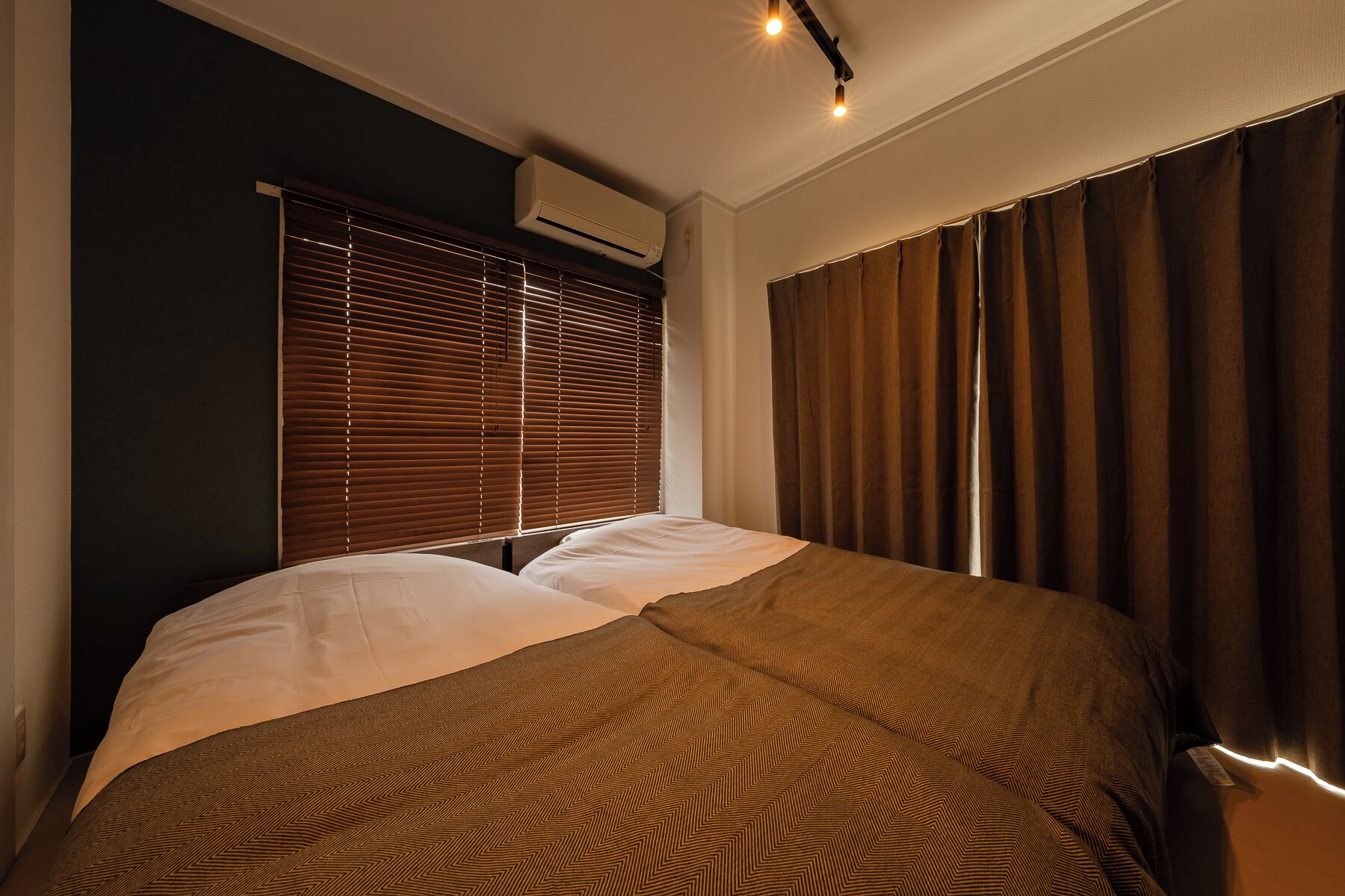 A bedroom with a bed, a window with blinds, a curtain, and an air conditioning unit.