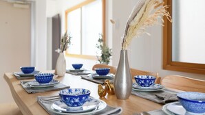 A dining table set with blue and white patterned bowls, a silver vase with dried plants, and gold decorative items.