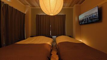 A hotel room with two beds, a large hanging light fixture, a television on the wall, and a window with curtains.