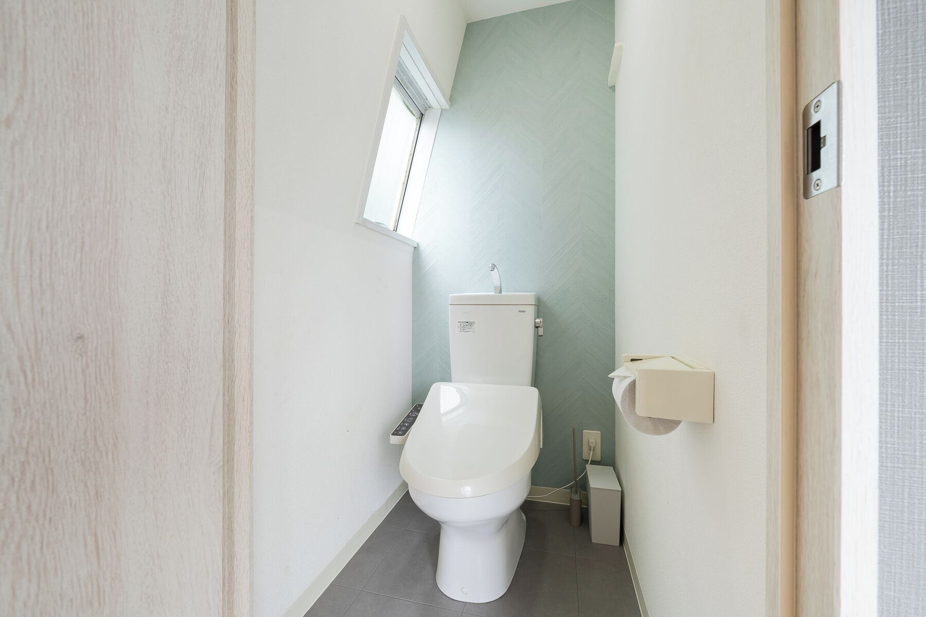 Une petite salle de bain étroite, comprenant des toilettes, un bidet fixé au mur et une fenêtre située au-dessus des toilettes.