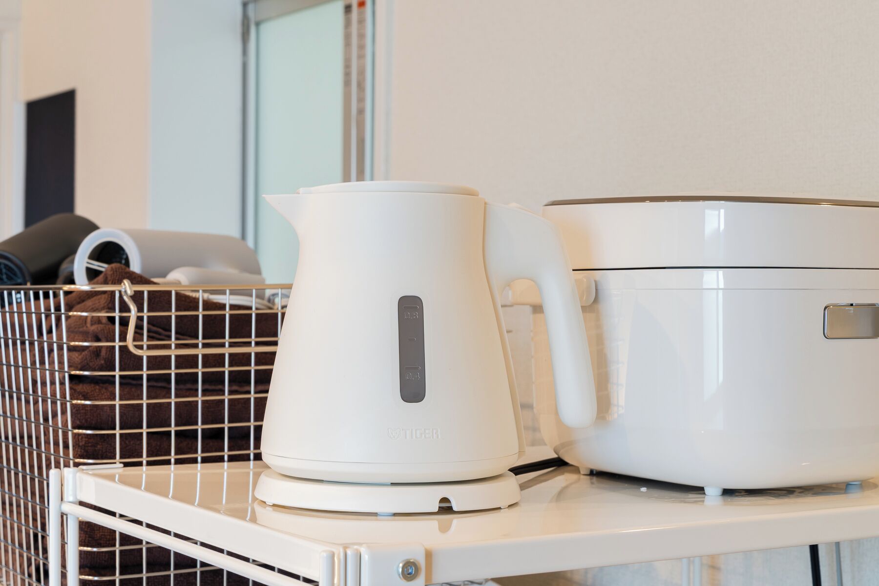 A white kettle and a white electric rice cooker on a white shelf.