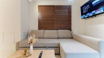 A modern living room with a beige sofa, a wooden coffee table, and a mounted TV displaying various streaming services.