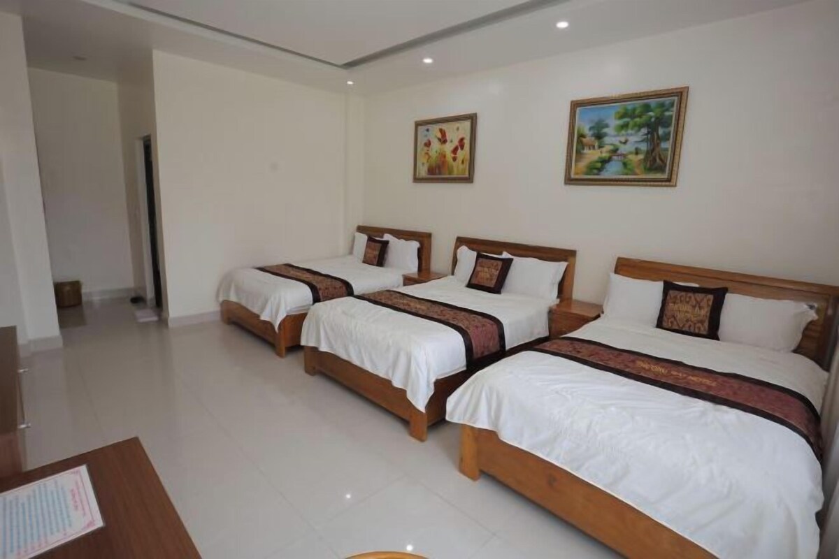 A hotel room with three single beds, a wooden desk, and two paintings on the wall.