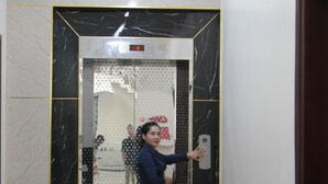 Una mujer parada en un ascensor, con un panel digital que muestra el número 1.