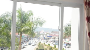 Vista desde una ventana a una calle concurrida, con palmeras y edificios.