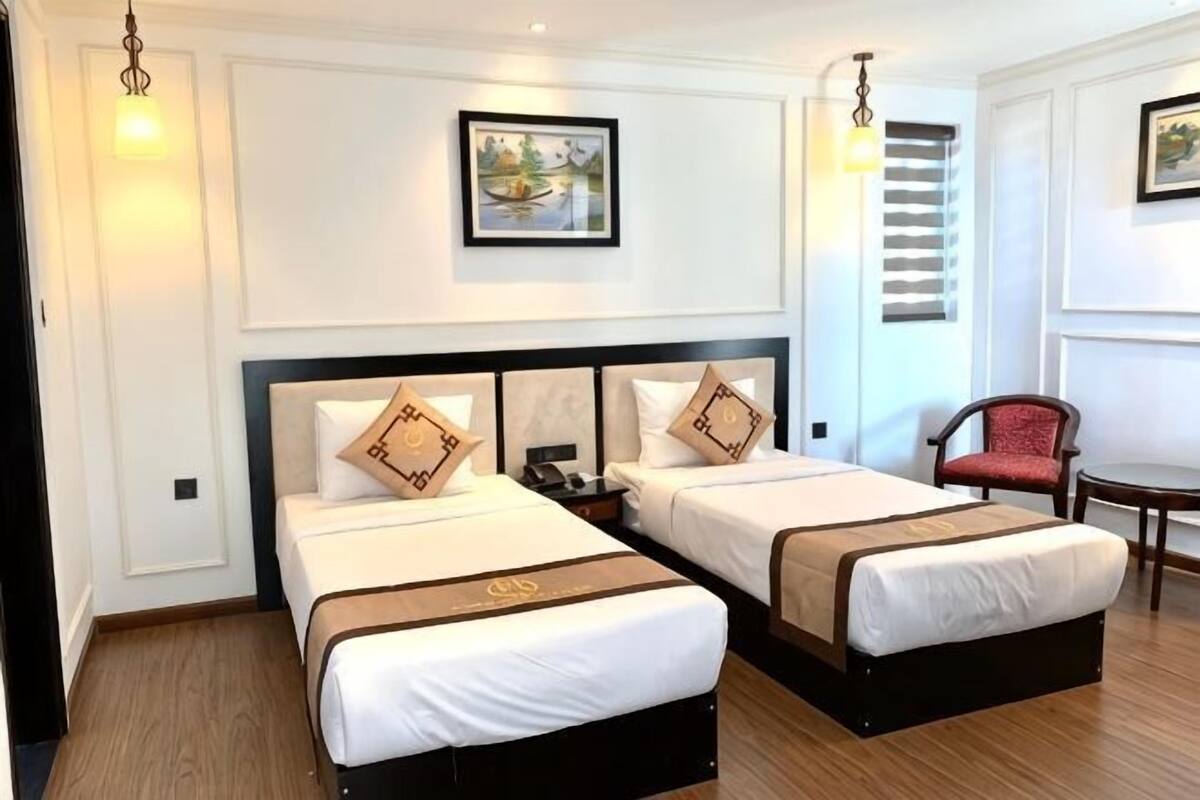 Habitació d'hotel amb dos llits, una cadira, una taula i un quadre penjat a la paret.