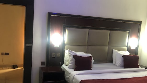 A hotel room with a large bed, two bedside tables, and a nightstand. There are two wall-mounted lights above the bed. - Mclorrets Suites (Enugu)