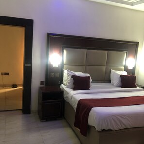A hotel room with a large bed, two bedside tables, and a nightstand. There are two wall-mounted lights above the bed. - Mclorrets Suites (Enugu)