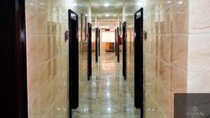A corridor with marble flooring and doors, leading to a room with a bed and a nightstand. - Mclorrets Suites (Enugu)