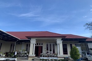 A two-story house with a red-tiled roof, a covered porch with potted plants, and a white exterior.