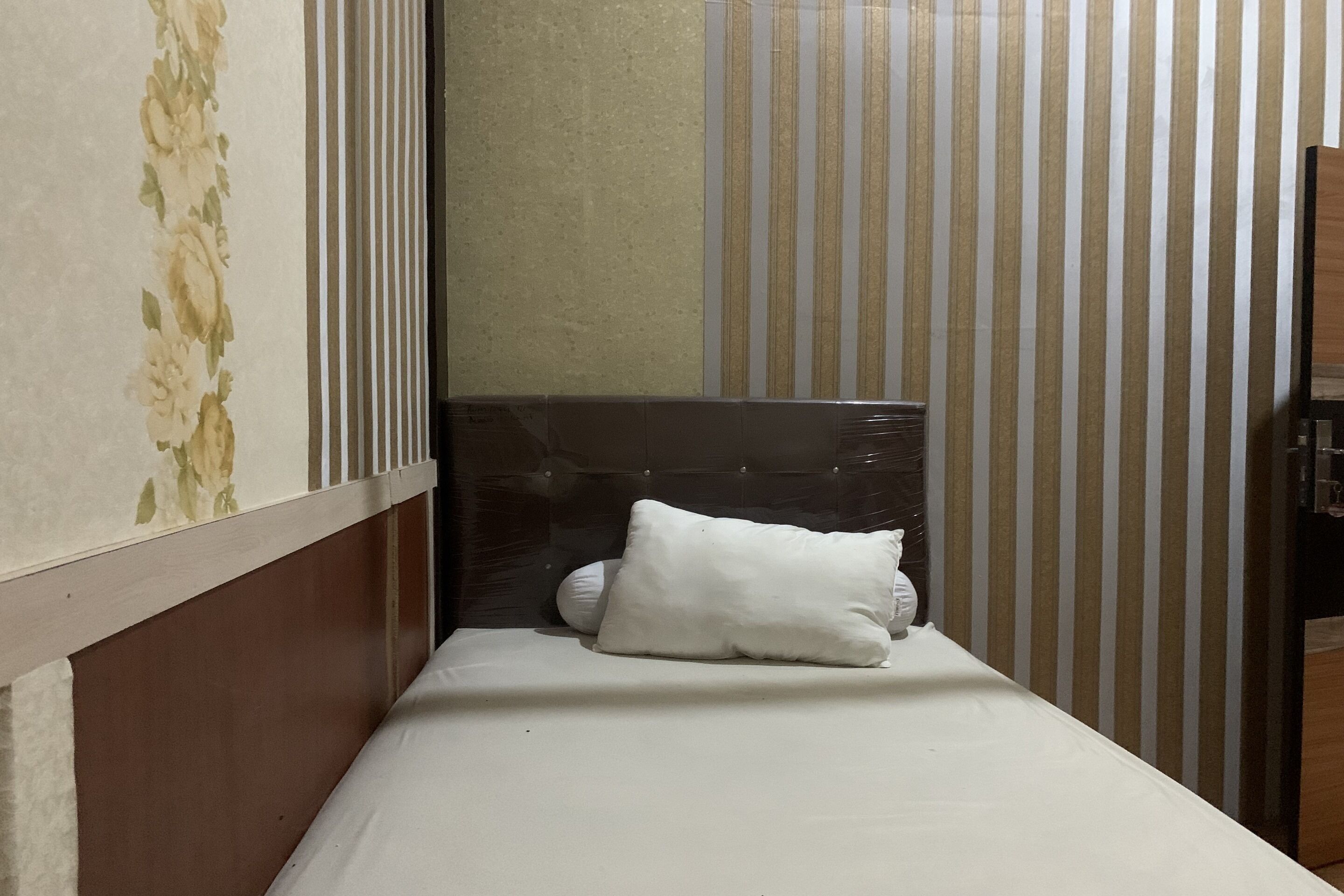A small, narrow room with a single bed, a headboard, and striped wallpaper.