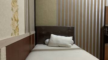 A small, narrow room with a single bed, a headboard, and striped wallpaper.