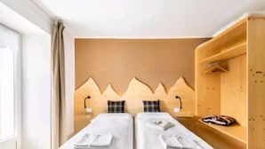 Una habitación con dos camas, cabecero de madera, estante con toallas y ventana con cortinas.
