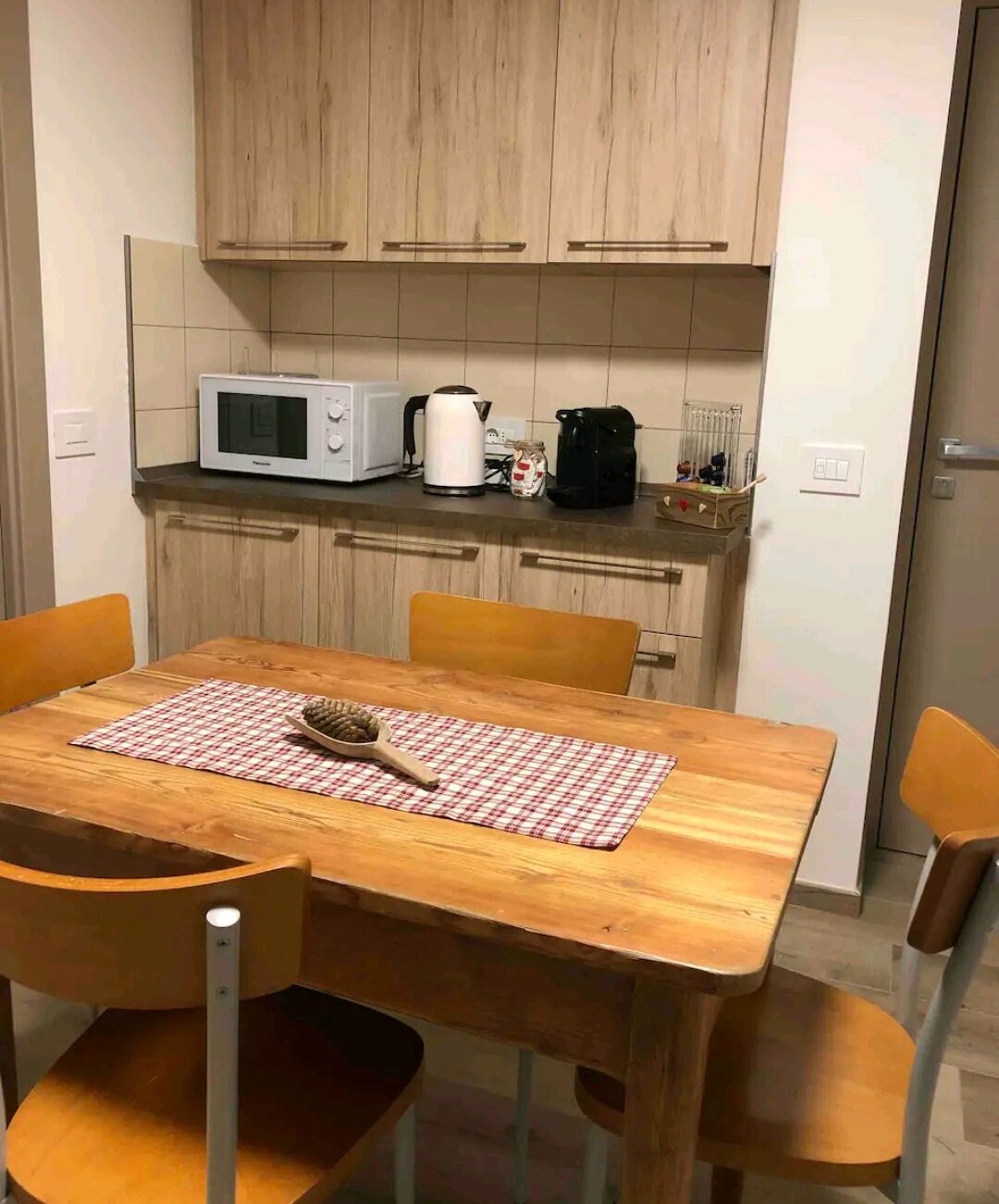 A compact kitchen with wooden cabinets, a microwave, a kettle, and a coffee maker on the countertop.
