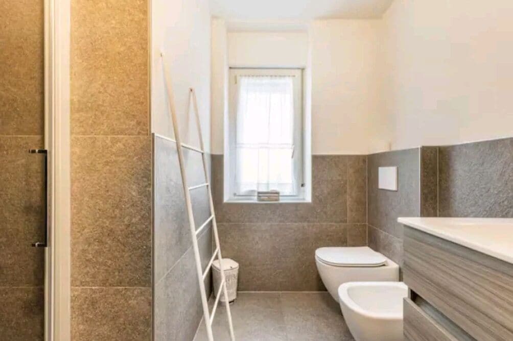 Un baño pequeño con inodoro, bidé y ventana con cortina.