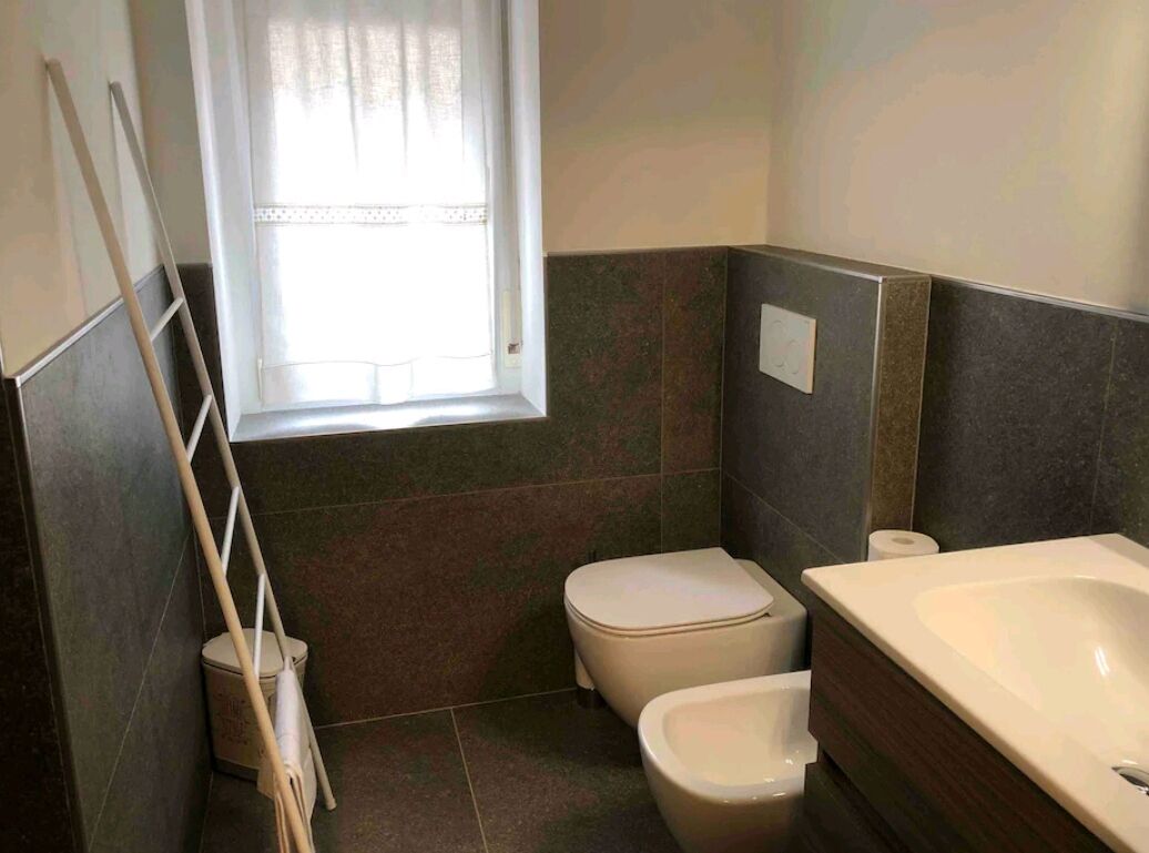 Uma casa de banho com duas sanitas, uma banheira, uma janela com cortinas e um esfregão encostado à parede.