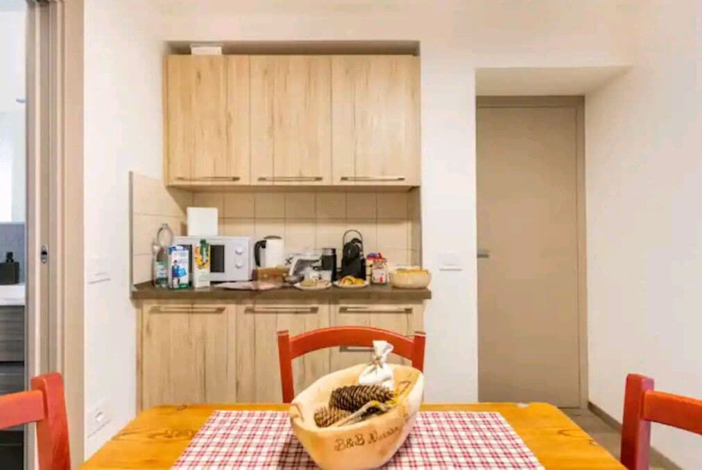 Een kleine keuken met houten kastjes, een magnetron en een tafel met geruit tafelkleed.