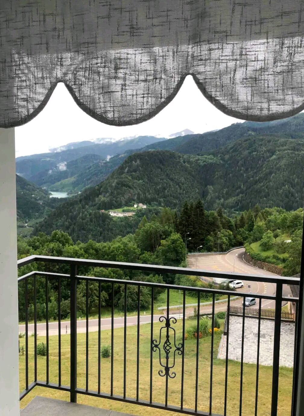 Un balcón con vista a un camino serpenteante y un valle con un lago.