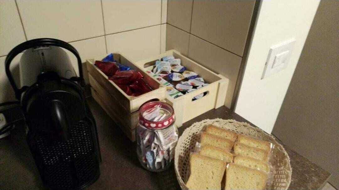 A kitchen area with a kettle, a jar of condiments, a basket of bread, and a wooden crate containing various packaged goods.