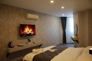 A modern hotel room with a flat-screen TV displaying a fireplace, a bedside table with a kettle and cups, a bed with a brown headboard, and a large window with curtains. - Cali Royal Otel (Denizli)