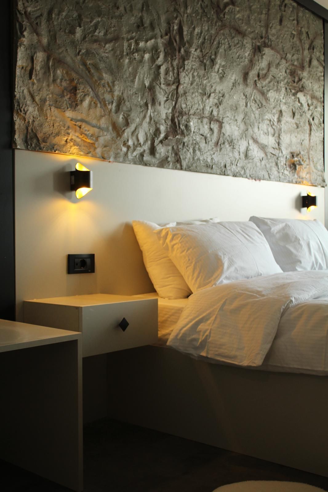 Un dormitorio con pared de piedra, una cama con ropa de cama blanca y dos mesitas de noche con lámparas.