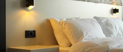 Un dormitorio con pared de piedra, una cama con ropa de cama blanca y dos mesitas de noche con lámparas.