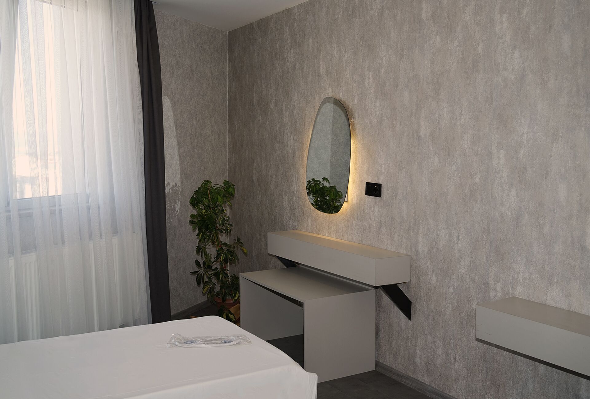 Un baño moderno con un espejo grande, una planta en maceta y un tocador blanco.